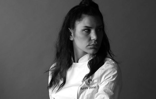 Ritratto in bianco e nero di Aurora Storari, pastry chef, in divisa da cucina, con sguardo fiero e deciso 