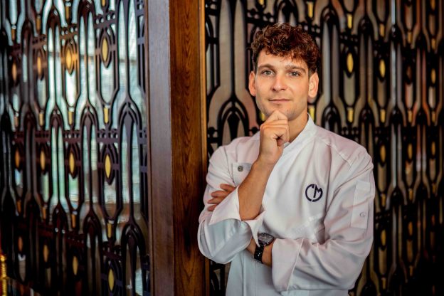 Mattia Casabianca in divisa bianca in posa nel ristorante con sfondo decorativo in legno e vetro